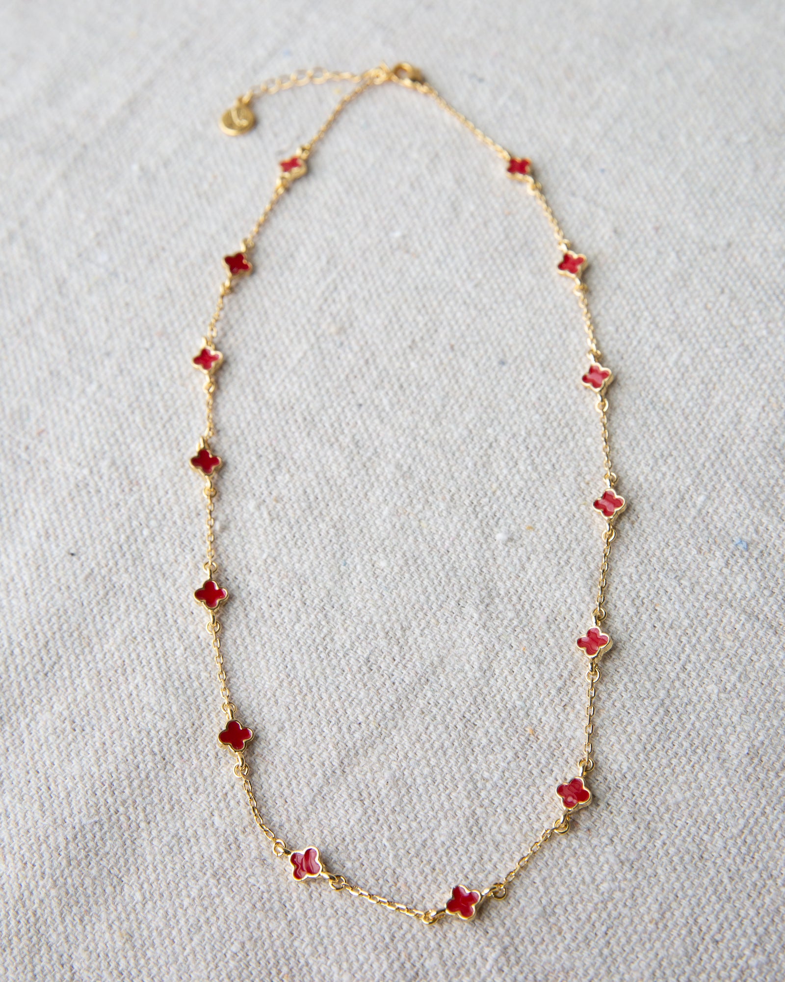 Gold necklace with red flower-shaped pendants on a light gray background