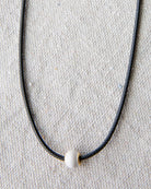 Necklace with a white bead on a textured beige background