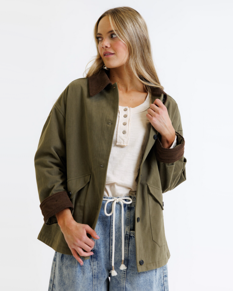 Woman wearing an olive green jacket with brown collar and cuffs on a white background