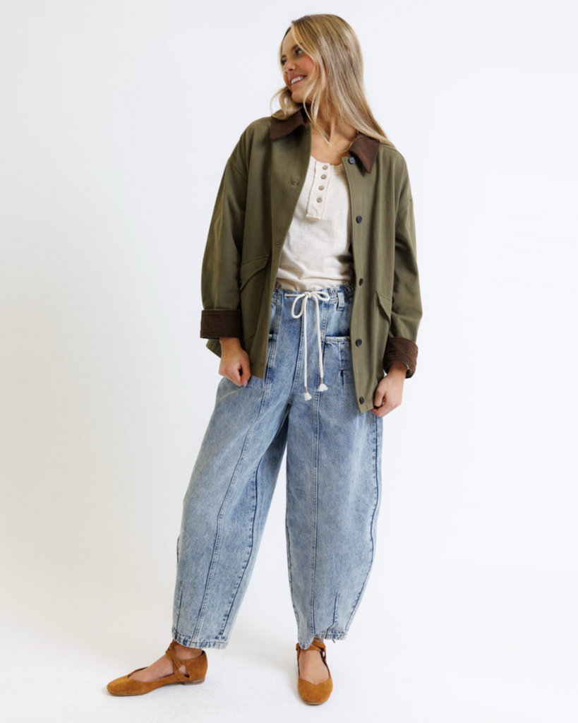 Woman wearing an olive green jacket, white shirt, and blue jeans on a white background