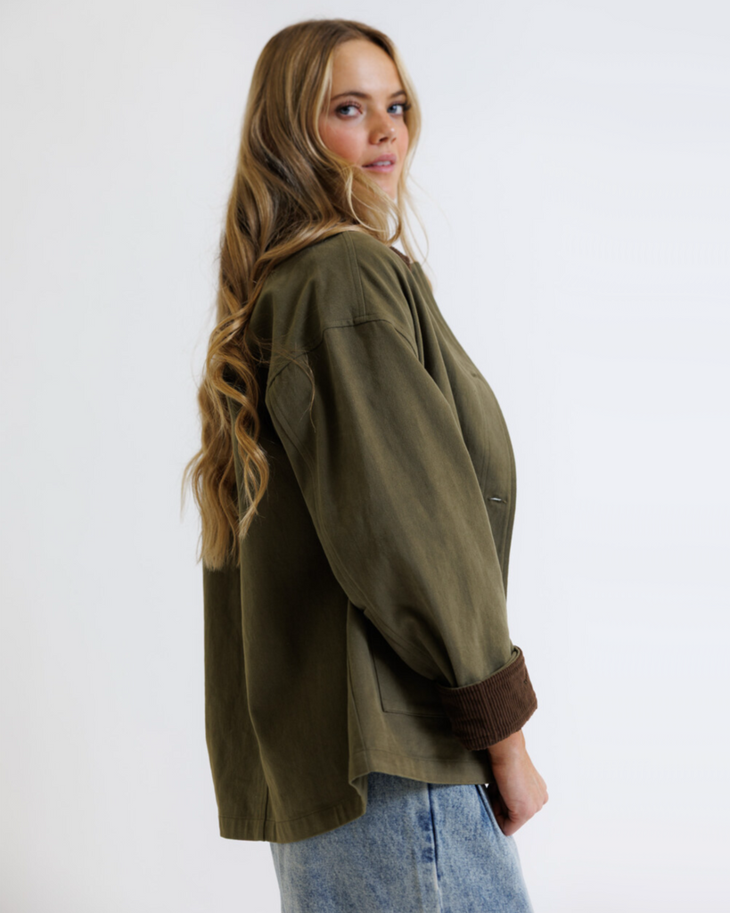 Woman wearing an olive green jacket and blue jeans on a white background