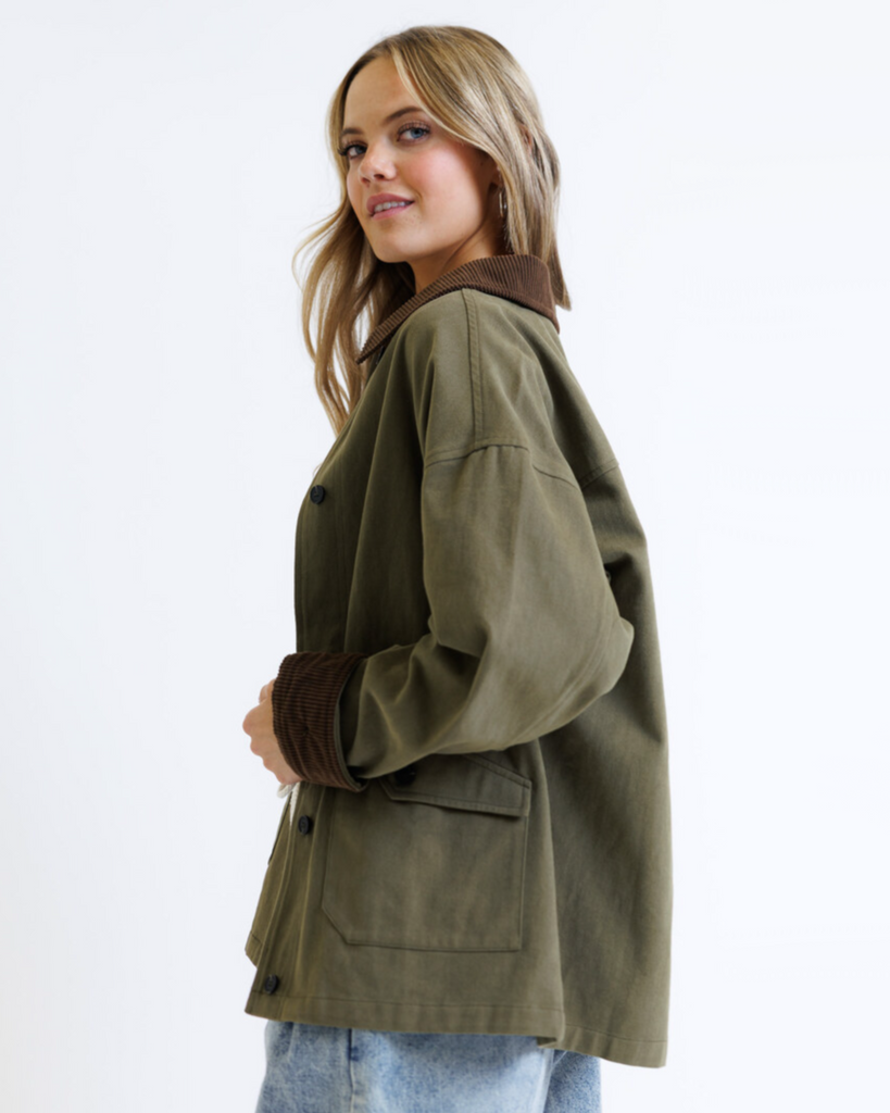 Woman wearing an olive green jacket with brown collar and cuffs on a white background