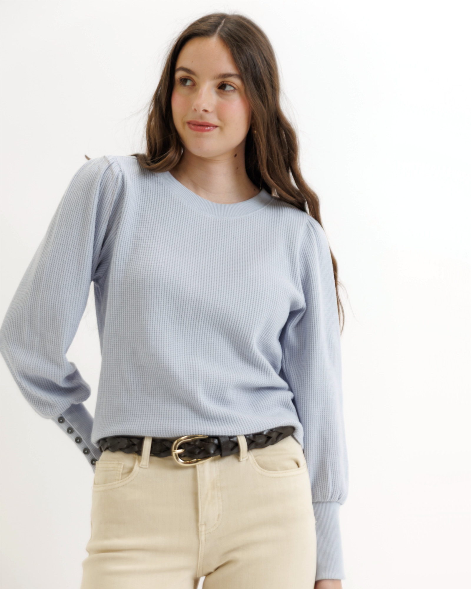 Woman wearing a light blue textured top and beige pants on a white background