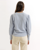 Woman wearing a light blue textured top and beige pants on a white background