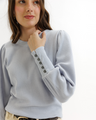 Woman wearing a light blue textured top and beige pants on a white background