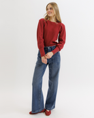 Woman wearing a red textured top and blue jeans on a white background