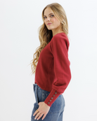 Woman wearing a red textured top and blue jeans on a white background