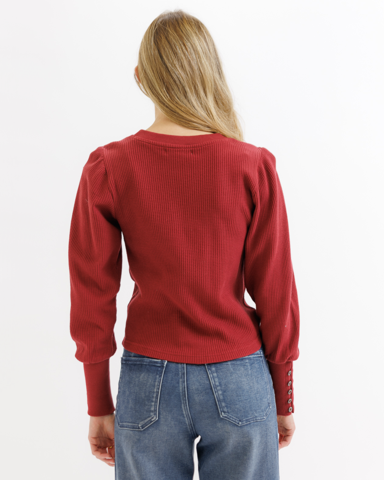 Woman wearing a red textured top and blue jeans on a white background
