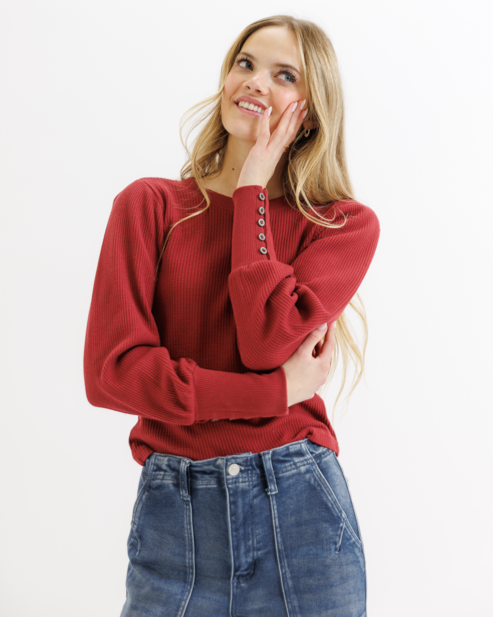 Woman wearing a red textured top and blue jeans on a white background