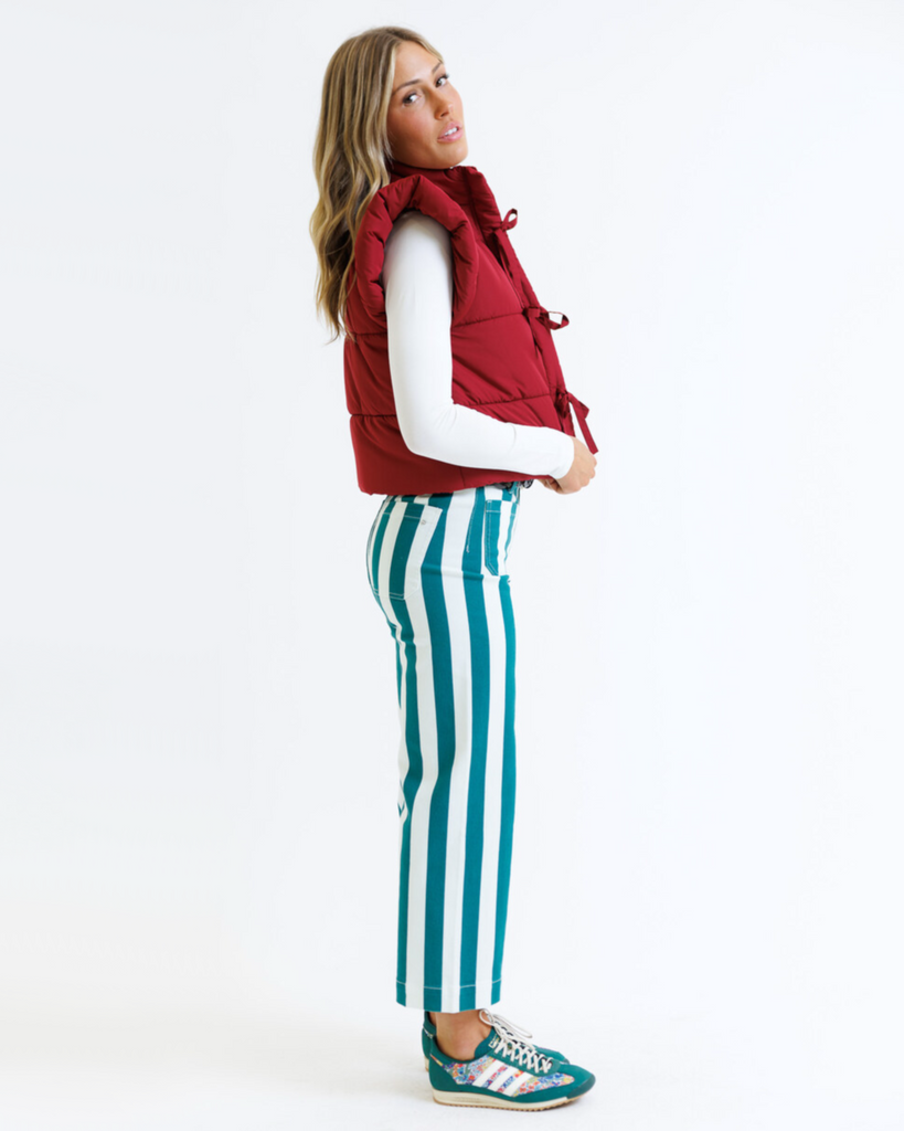 Woman wearing a red puffer vest and striped pants on a white background