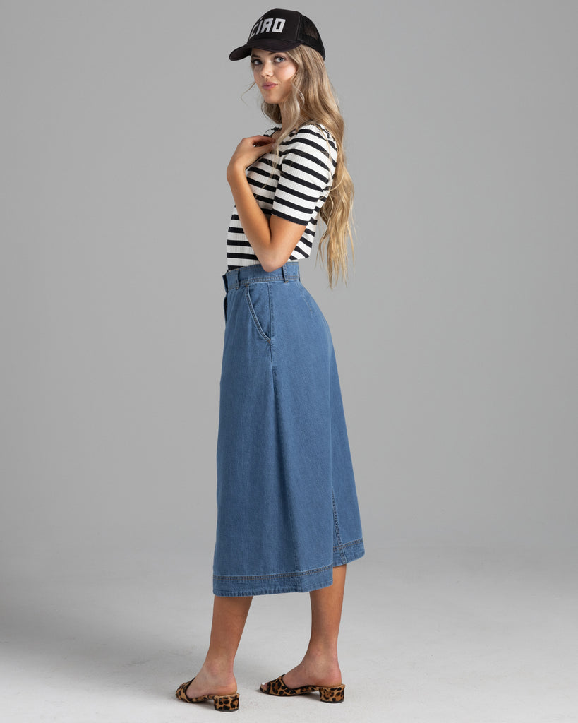 Model wearing a blue denim a-line midi length skirt with buttons down the front.