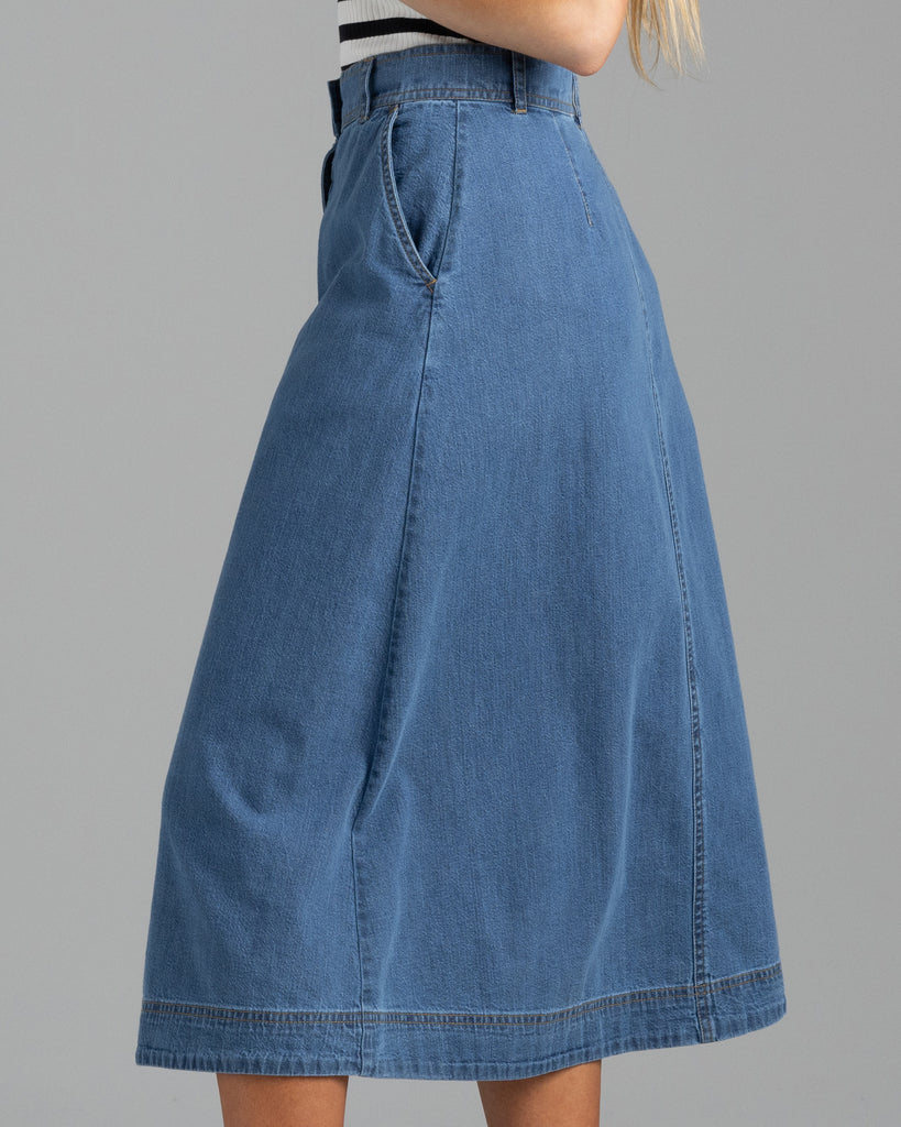 Model wearing a blue denim a-line midi length skirt with buttons down the front.