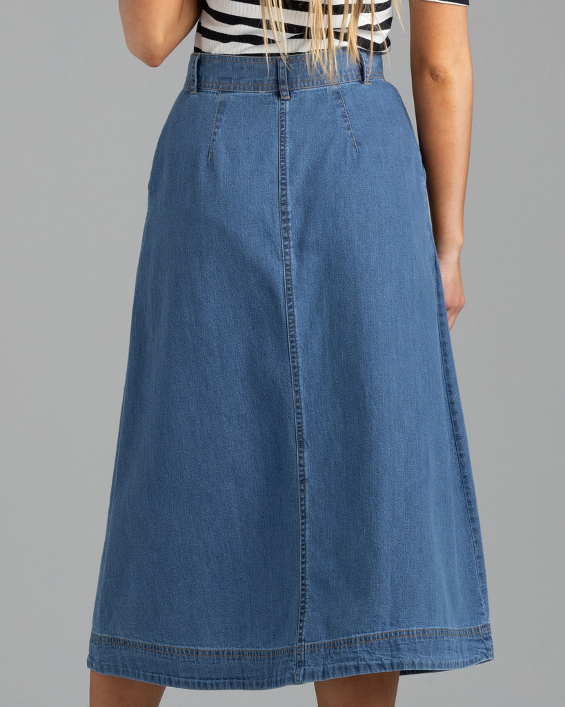 Model wearing a blue denim a-line midi length skirt with buttons down the front.