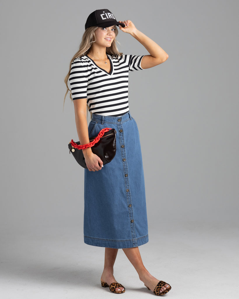 Model wearing a blue denim a-line midi length skirt with buttons down the front.