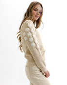 Woman wearing a beige sweater with white floral patterns on a white background