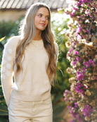 Woman in a beige sweater standing in front of flowers