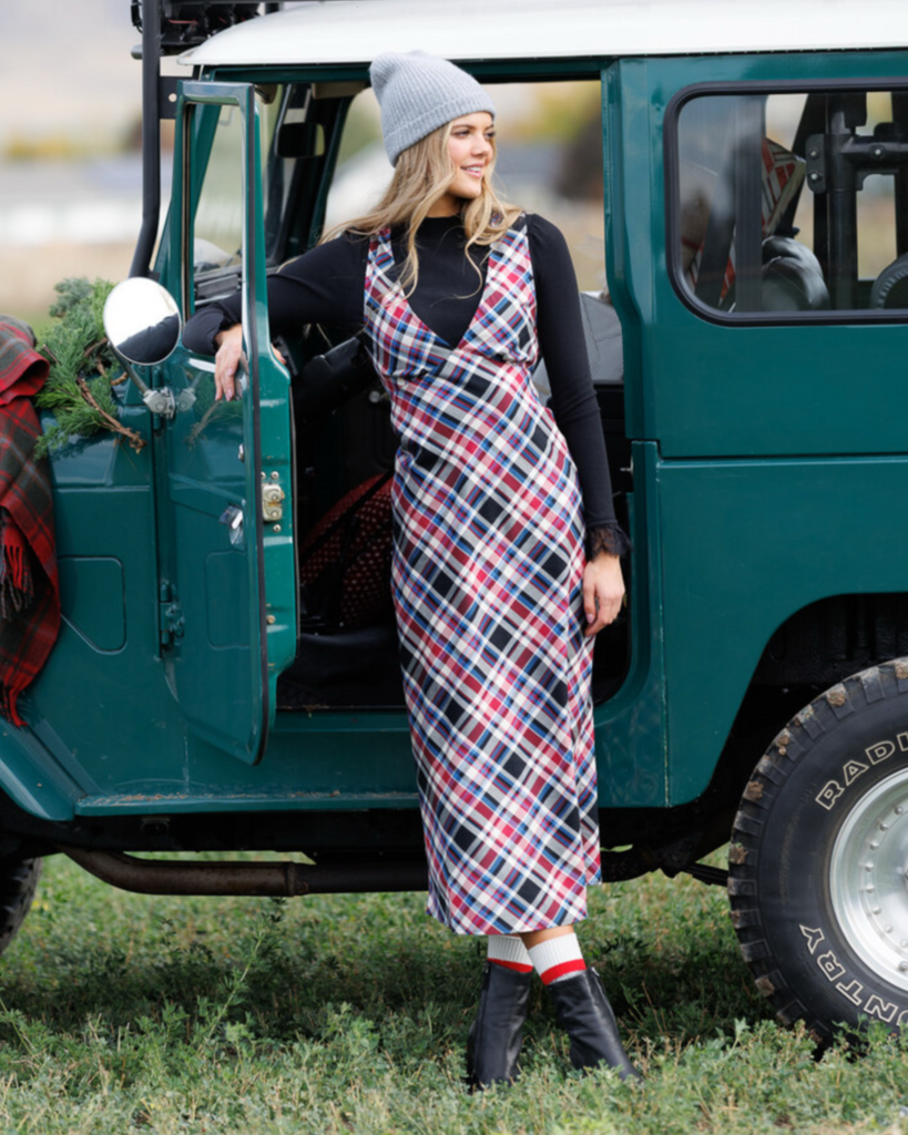 Woman in a plaid dress standing next to a green car
