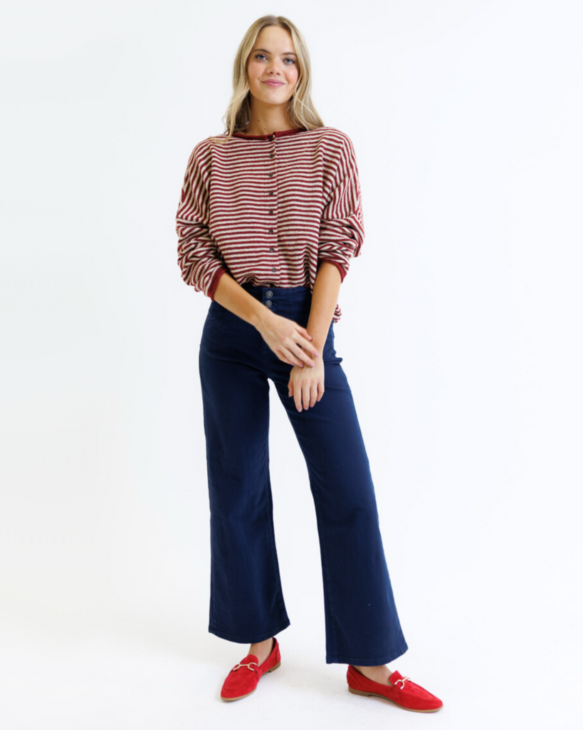 Woman wearing a striped cardigan, navy pants, and red shoes on a white background