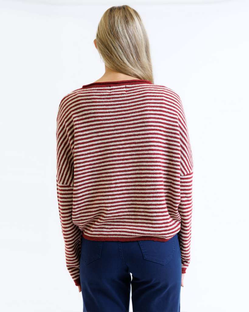 Person wearing a red and white striped sweater with blue pants on a white background