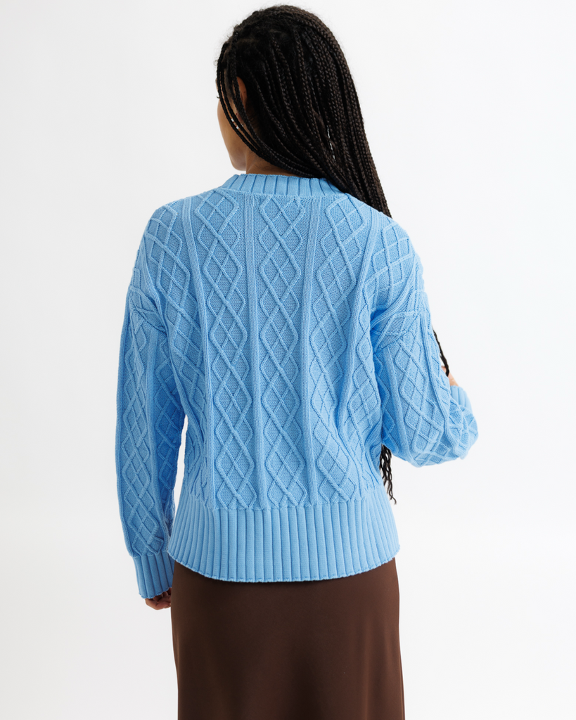 Person wearing a light blue cable knit sweater on a white background