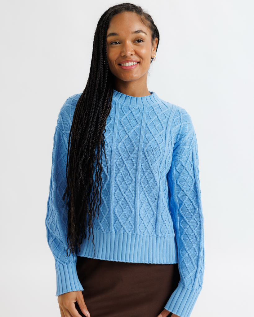Woman wearing a blue cable knit sweater against a plain background