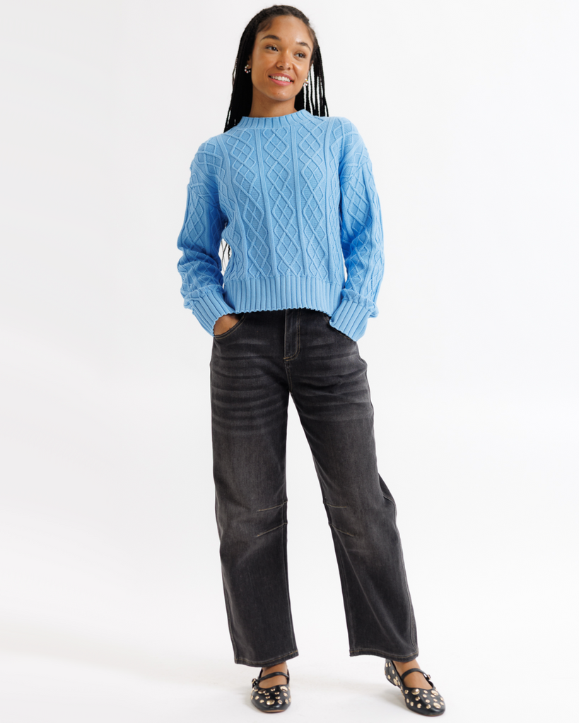 Person wearing a blue cable knit sweater and black jeans on a white background