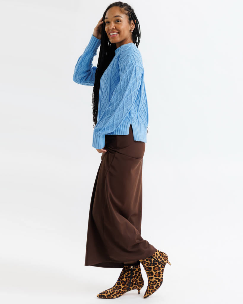 Woman wearing a blue sweater and brown pants with leopard print boots on a white background