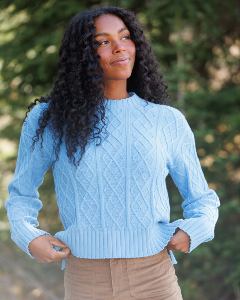 Woman wearing a light blue cable knit sweater in the forest