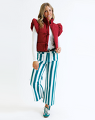Woman wearing a red puffer vest and green striped pants on a white background