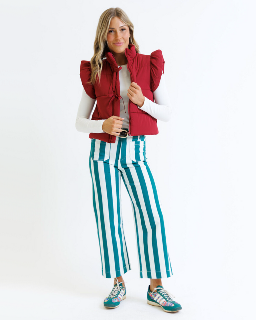 Woman wearing a red puffer vest and green striped pants on a white background