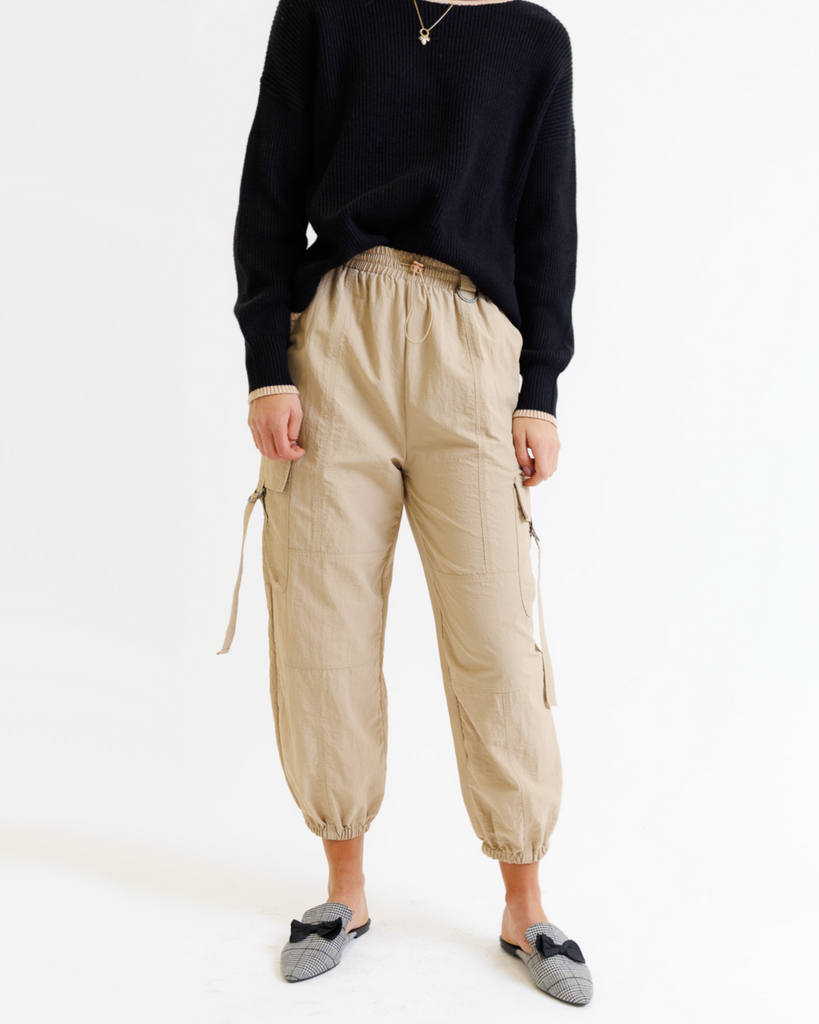 Woman wearing a black sweater and taupe cargo pants on a white background