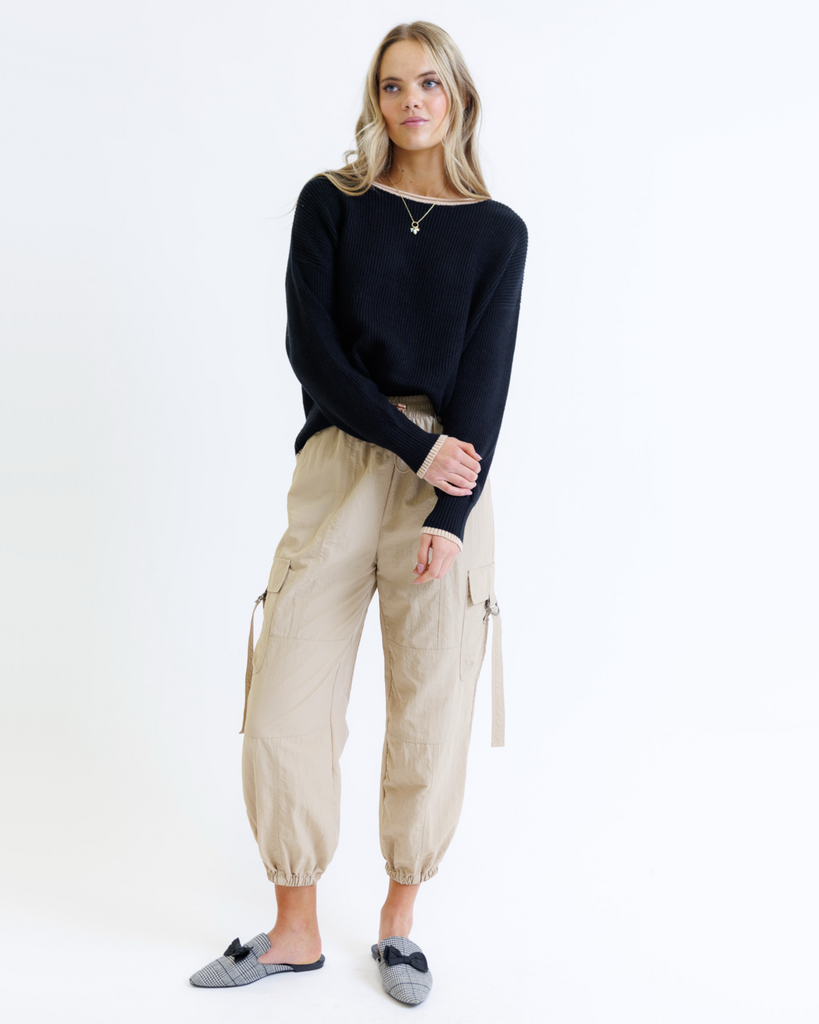 Woman wearing a black sweater and taupe cargo pants on a white background