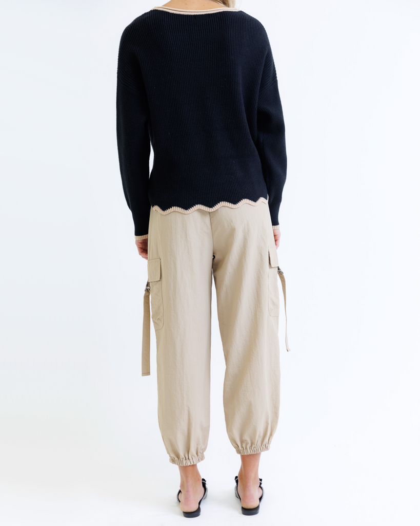 Woman wearing a black sweater and taupe cargo pants on a white background