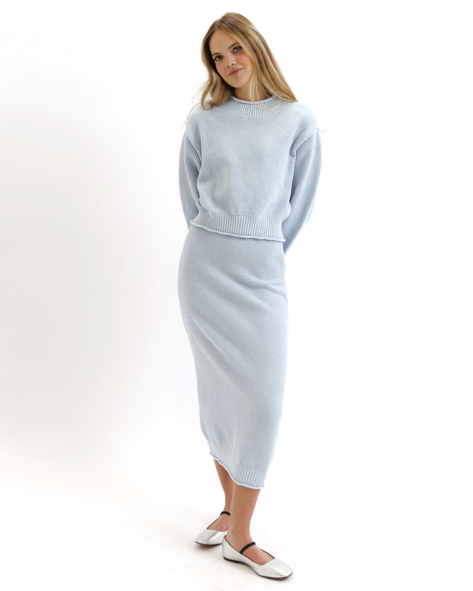 Woman wearing a light blue knitted sweater and skirt set on a white background
