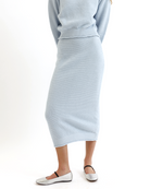 Woman wearing a light blue knitted sweater and skirt set on a white background