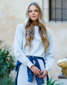 Woman wearing a light blue sweater with a denim jacket tied around her waist outdoors.
