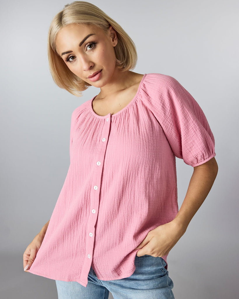 Woman in a short sleeved, pink blouse with buttons down the front and slight texturing of material