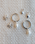 Set of silver hoop earrings with miscellaneous charms on a textured beige surface