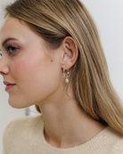 Close-up of a woman wearing silver hoop earrings with a pearl charm on a neutral background