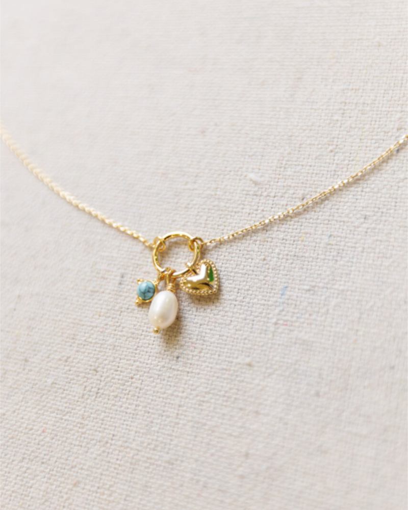 Delicate gold necklace with a heart charm, pearl, and blue gemstone on a light gray background