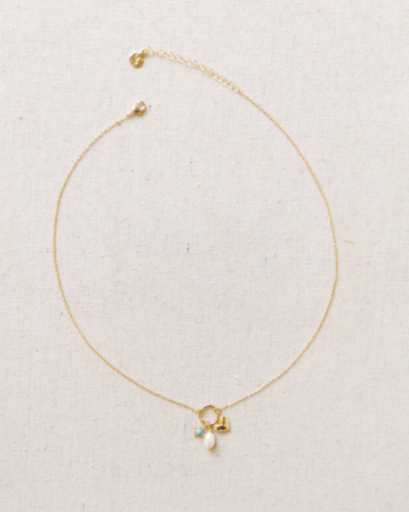 Delicate gold necklace with a heart charm, pearl, and blue gemstone on a light gray background