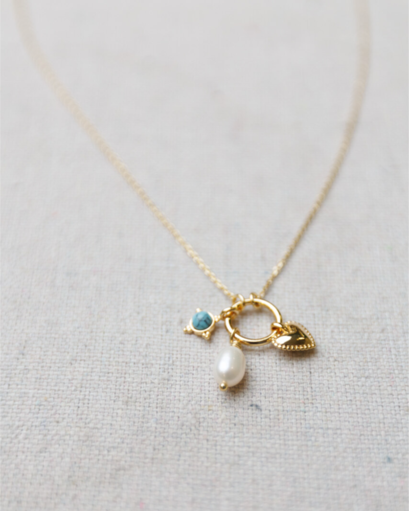 Delicate gold necklace with a heart charm, pearl, and blue gemstone on a light gray background