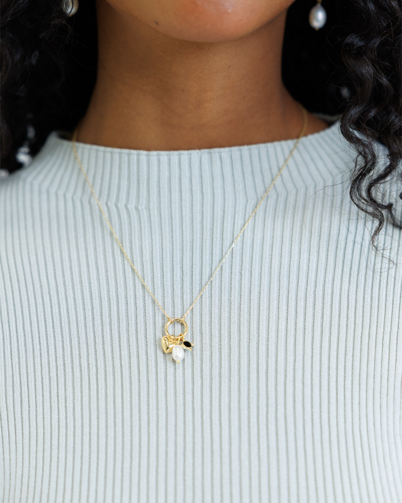 Woman wearing gold necklace with charms and a blue ribbed shirt