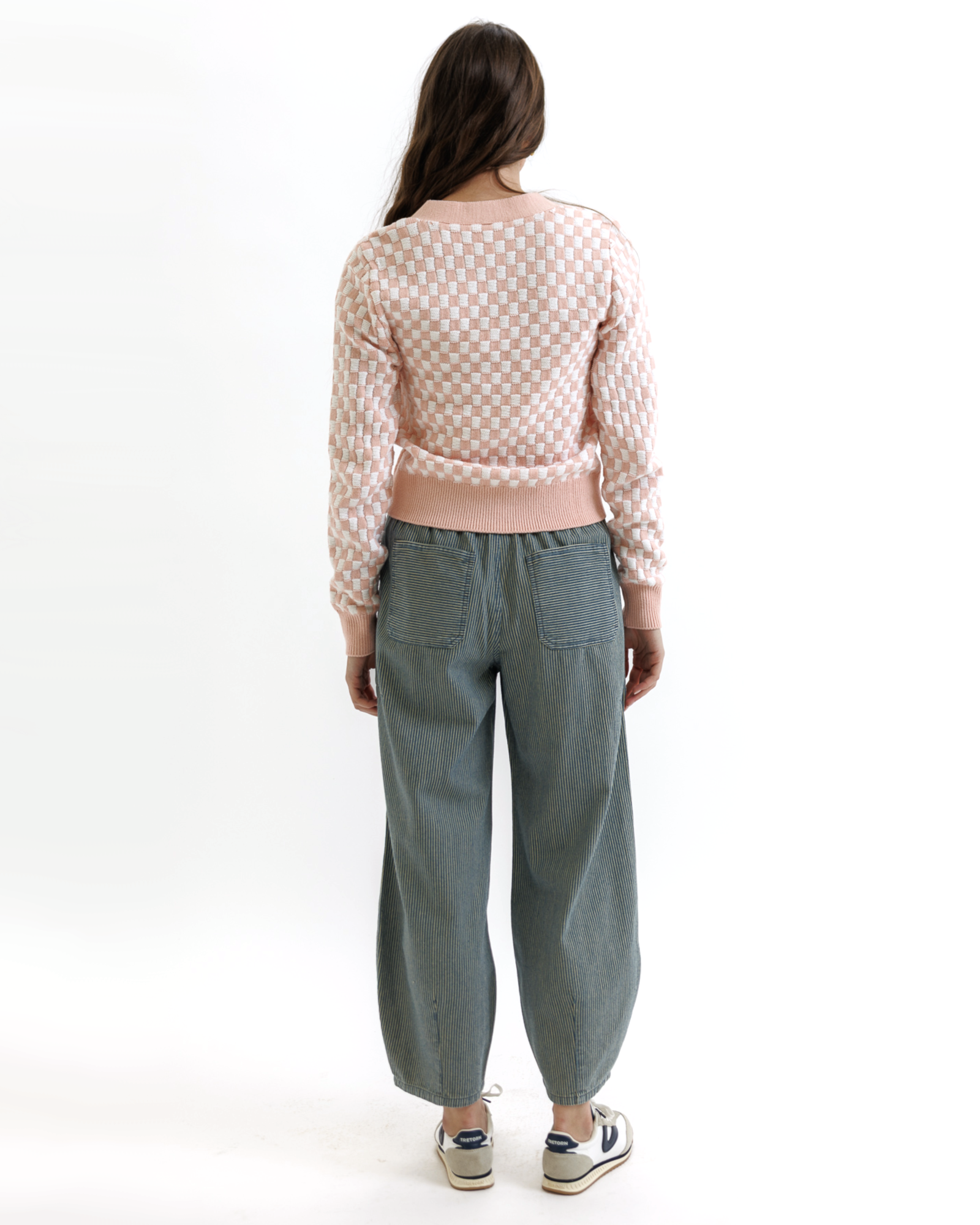 Woman wearing a pink checkered cardigan with buttons and gray pants on a white background