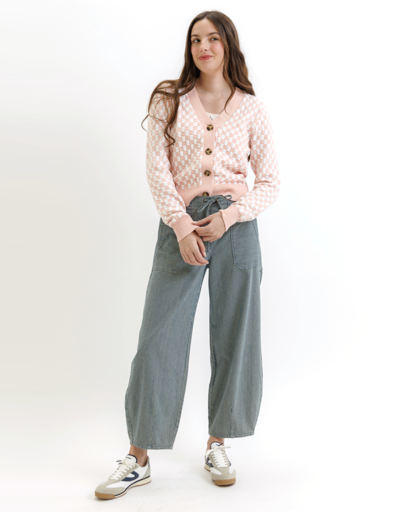 Woman wearing a pink checkered cardigan with buttons and gray pants on a white background