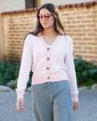 Woman wearing a pink checkered cardigan with buttons standing in front of a brick wall.