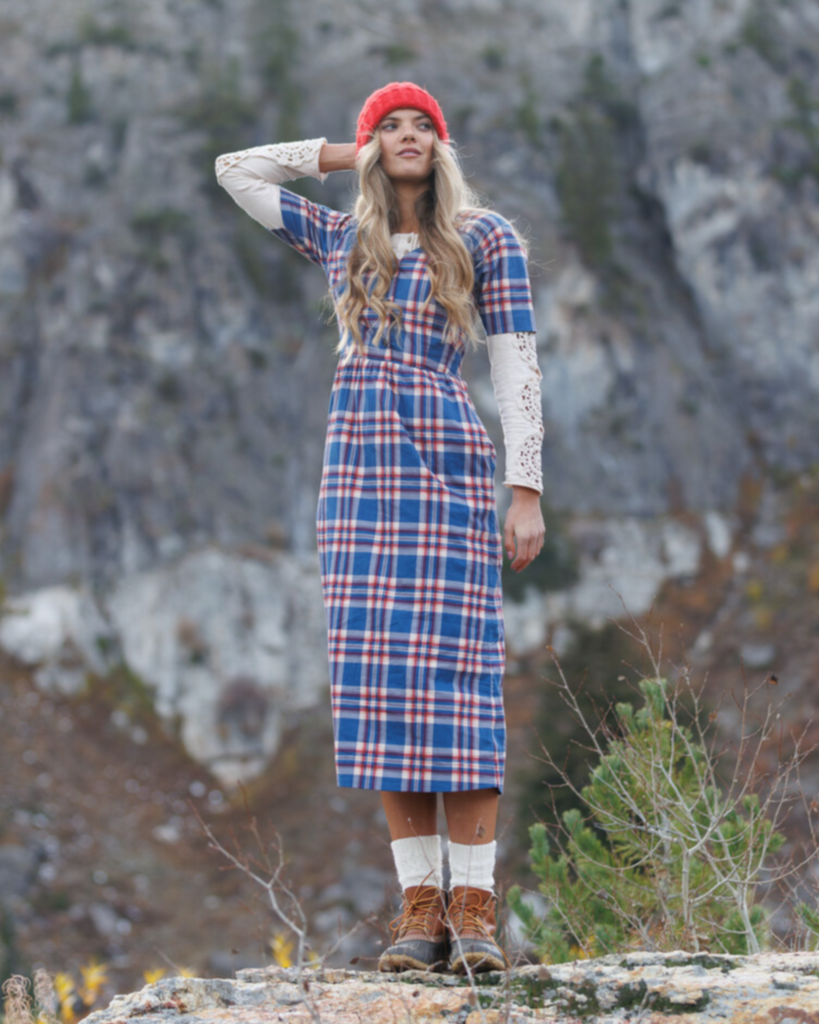 Woman in a plaid dress and red beanie standing in a mountainous landscape