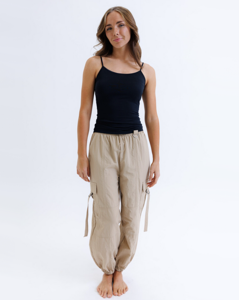 Woman wearing a black layering tank top and tan cargo pants against a white background