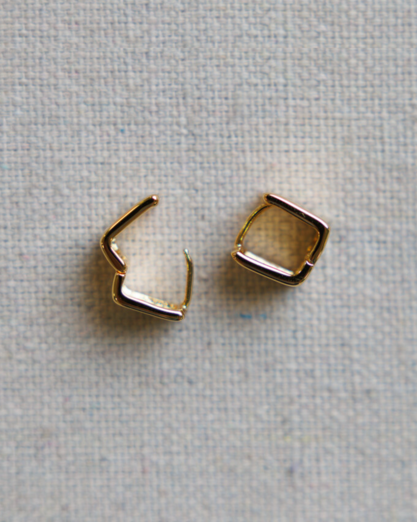 Two gold square hoop earrings on a textured gray background