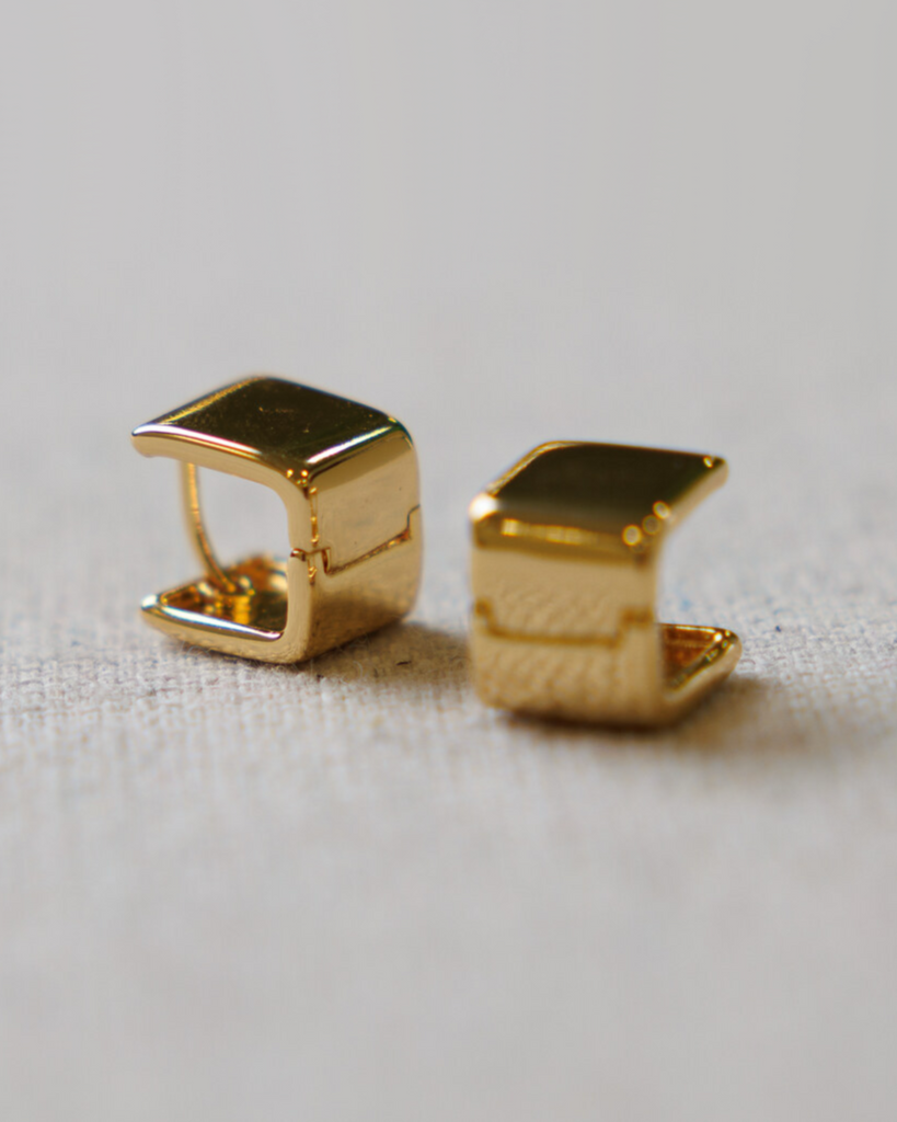 Two gold square hoop earrings on a textured gray background